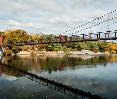 Swinging pedestrian bridge over the Androscoggin River in Brunswick, Maine with fall foliage