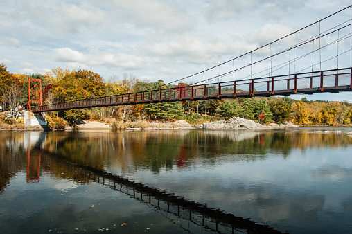 Swinging pedestrian bridge over the Androscoggin River in Brunswick, Maine with fall foliage